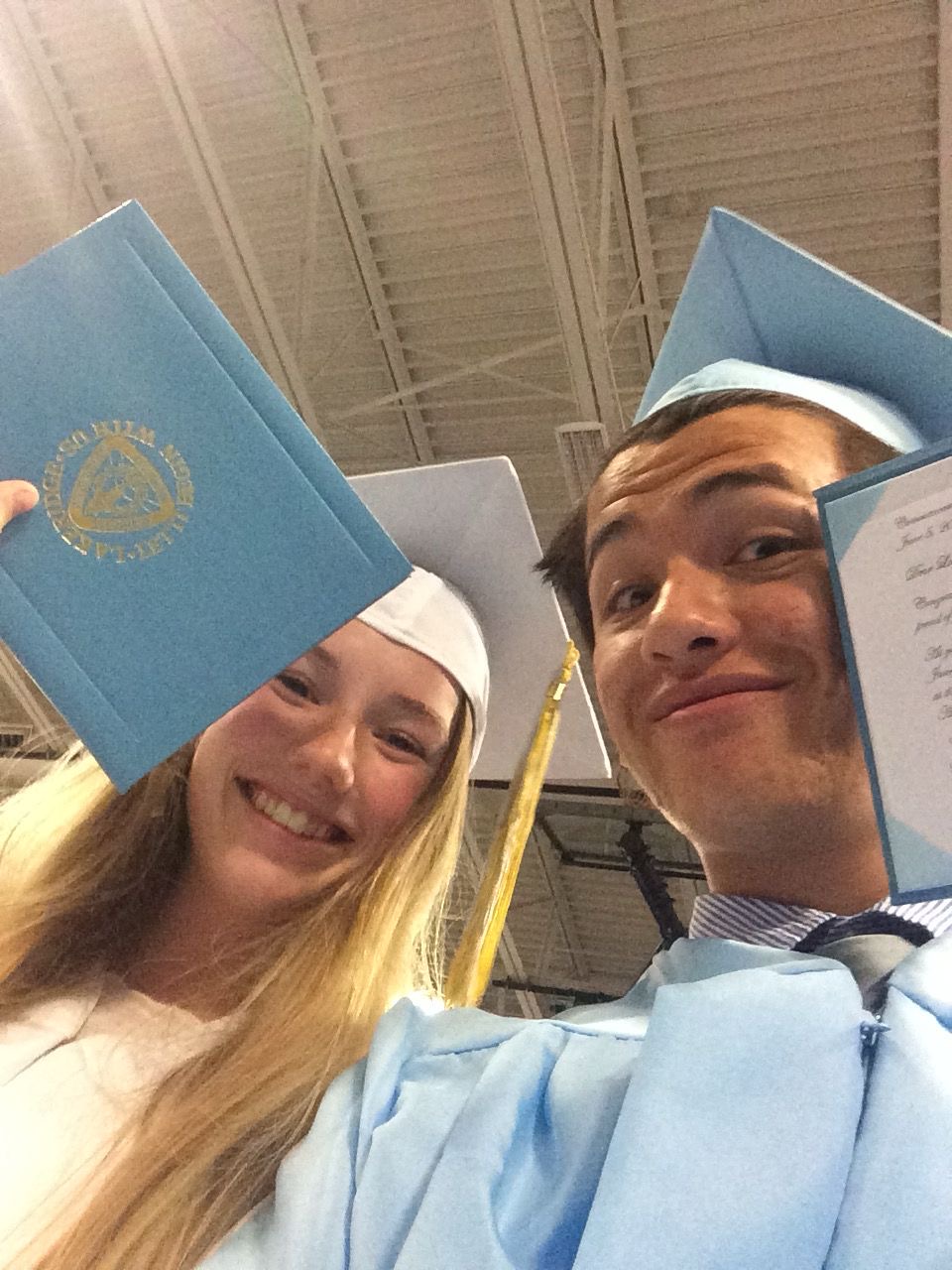 Alex and a classmate at graduation holding diplomas